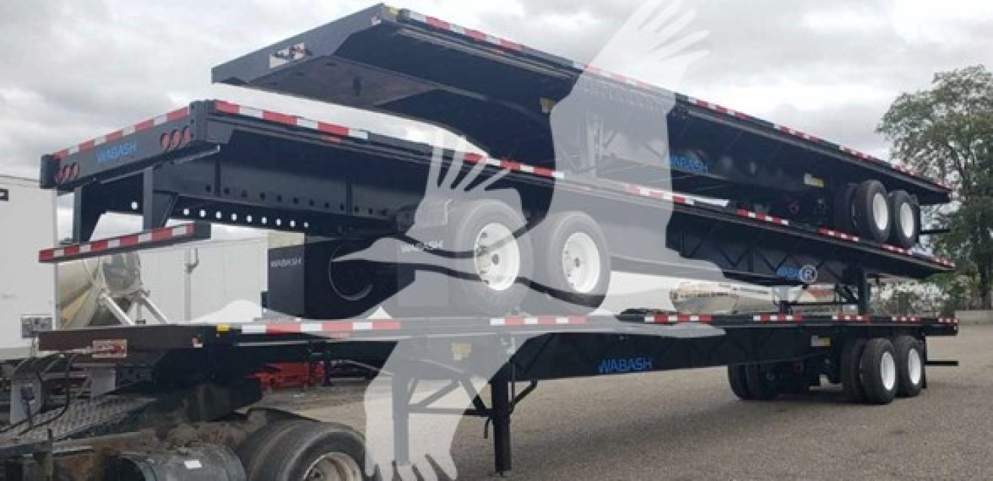 Flatbed trailer in-service showing steel air slider with dual rear axles and wood deck, side text and reflective striping.