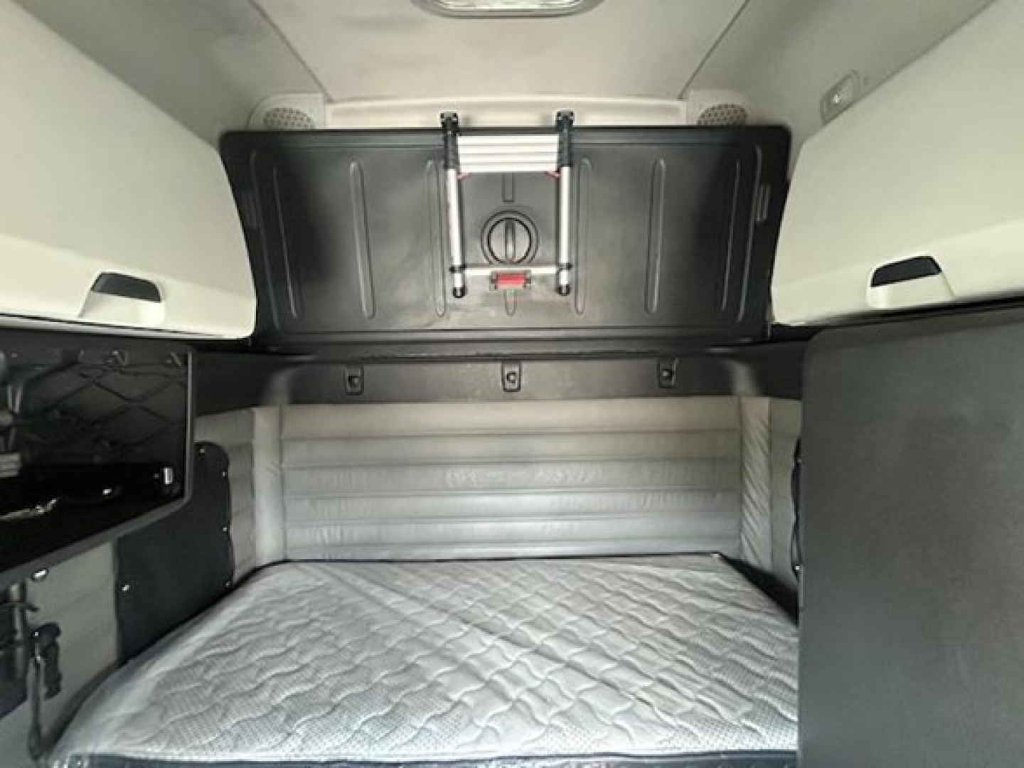 Freightliner Cascadia sleeper cab interior showing rear bunk area with quilted mattress and storage panels.