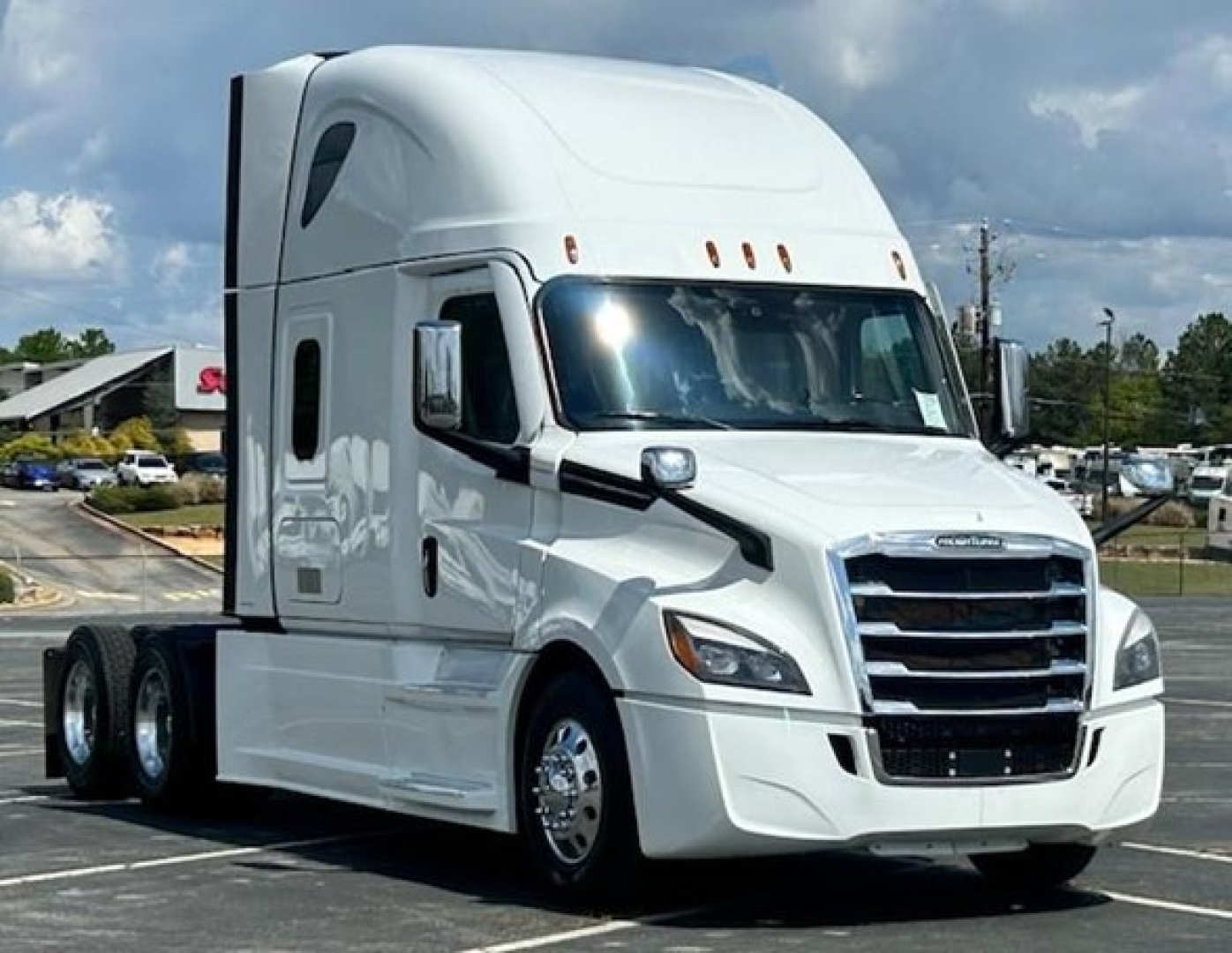 A white Freightliner Cascadia 126 tractor-trailer in a parking lot, showing the cab with a prominent grille and three roadside clearance lights; no visible text on the vehicle.