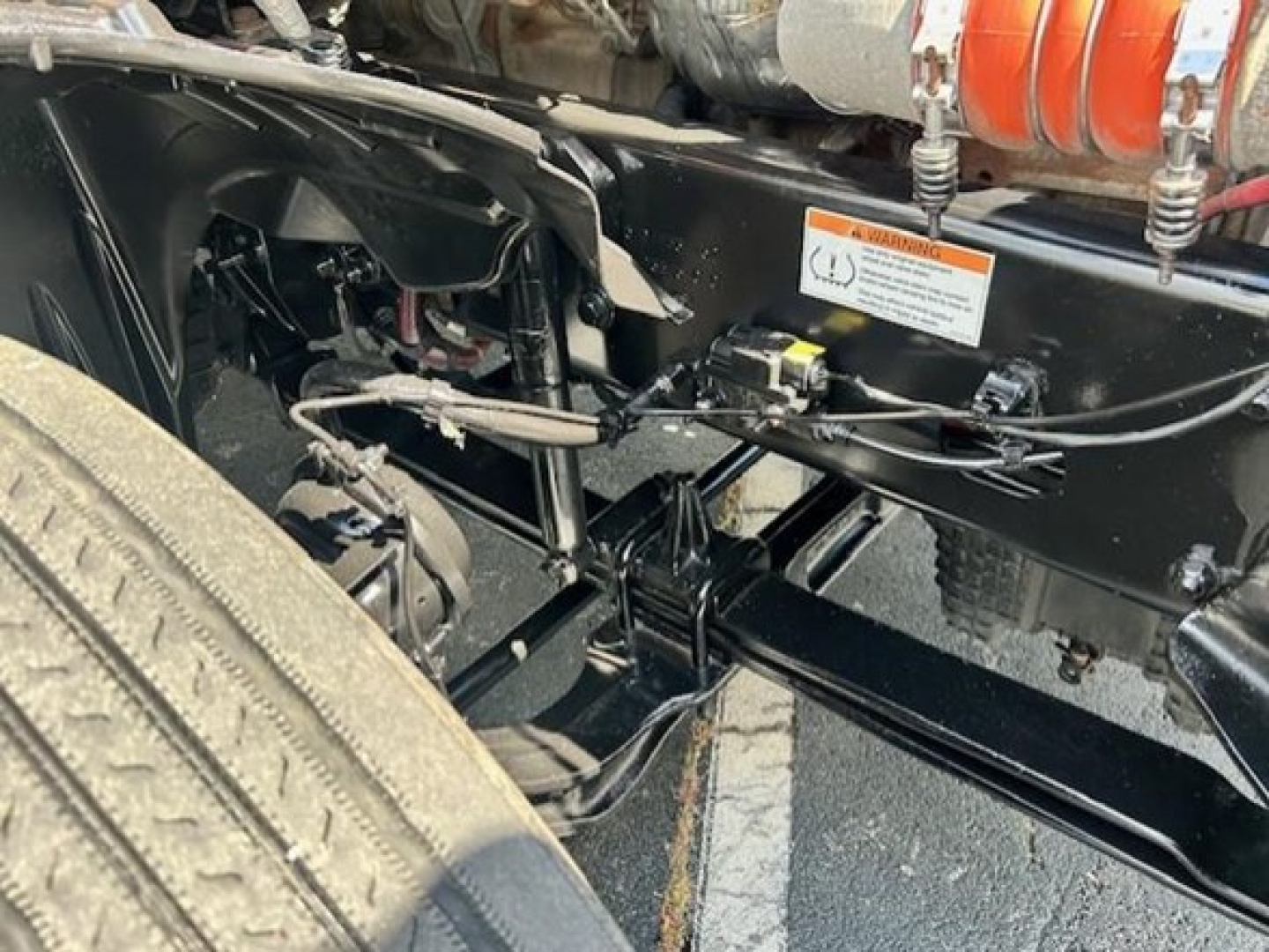 Cascadia truck chassis showing undercarriage components, hoses, and frame with warning sticker visible.