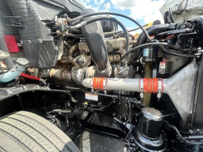 Engine bay of a Freightliner Cascadia 126 showing coolant reservoir, air intake, hoses, and battery with engine components visible.