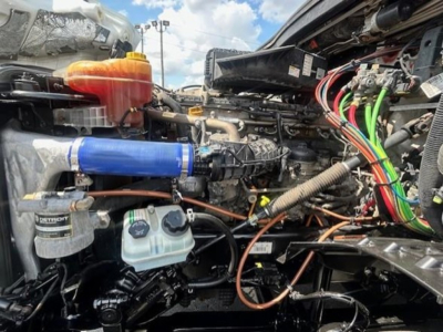 Freightliner Cascadia engine bay showing various components including coolant reservoir, hoses, wiring harness, and air intake with blue silicone coupler.