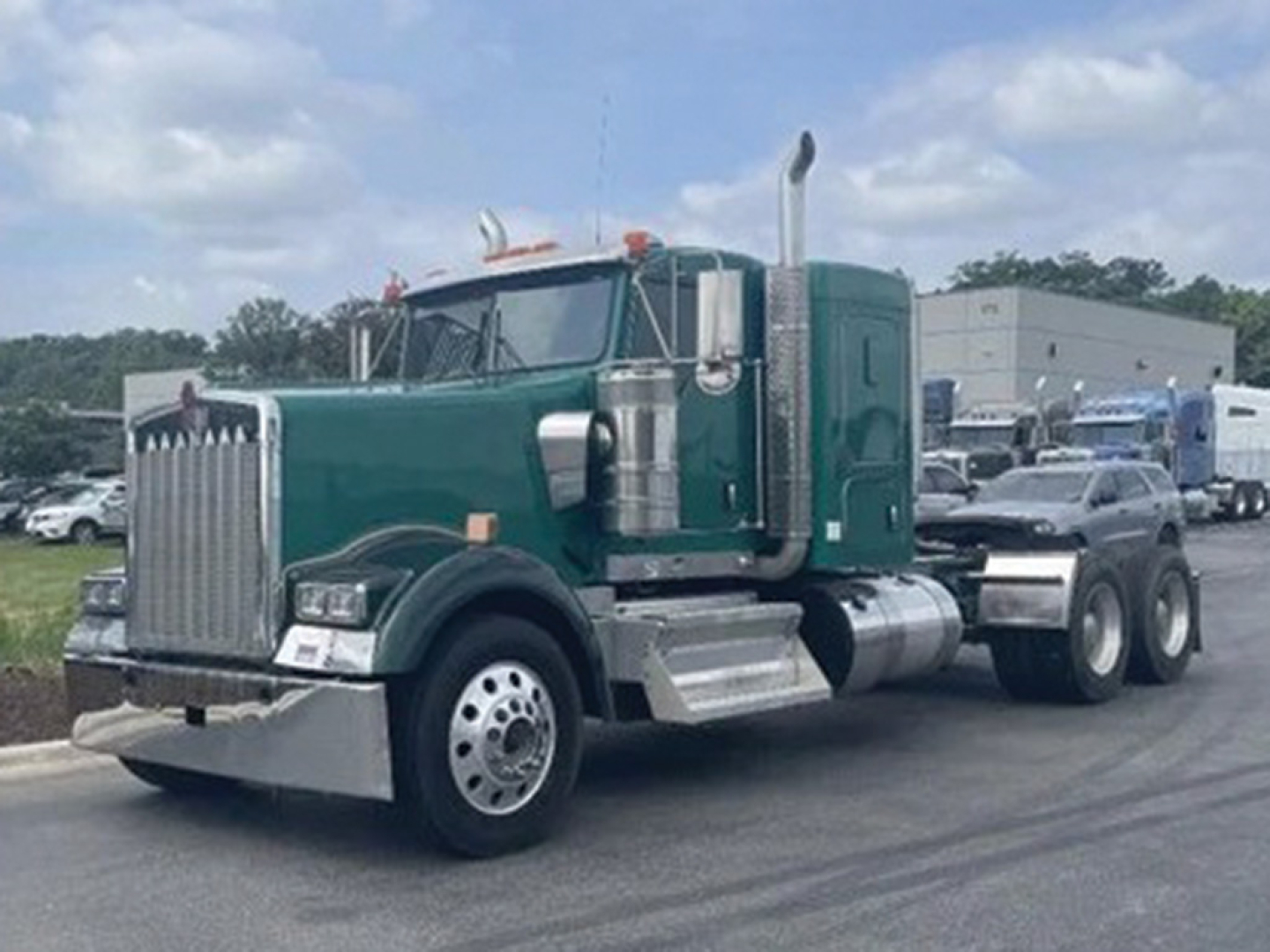 Kenworth W-900 conventional sleeper tractor in green with chrome exhaust stacks and large grille, front-left view showing dual rear axles.