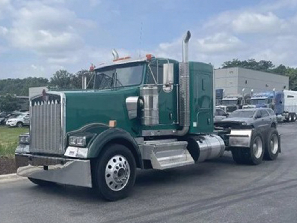 Kenworth W-900 conventional sleeper tractor in green with chrome exhaust stacks and large grille, front-left view showing dual rear axles.