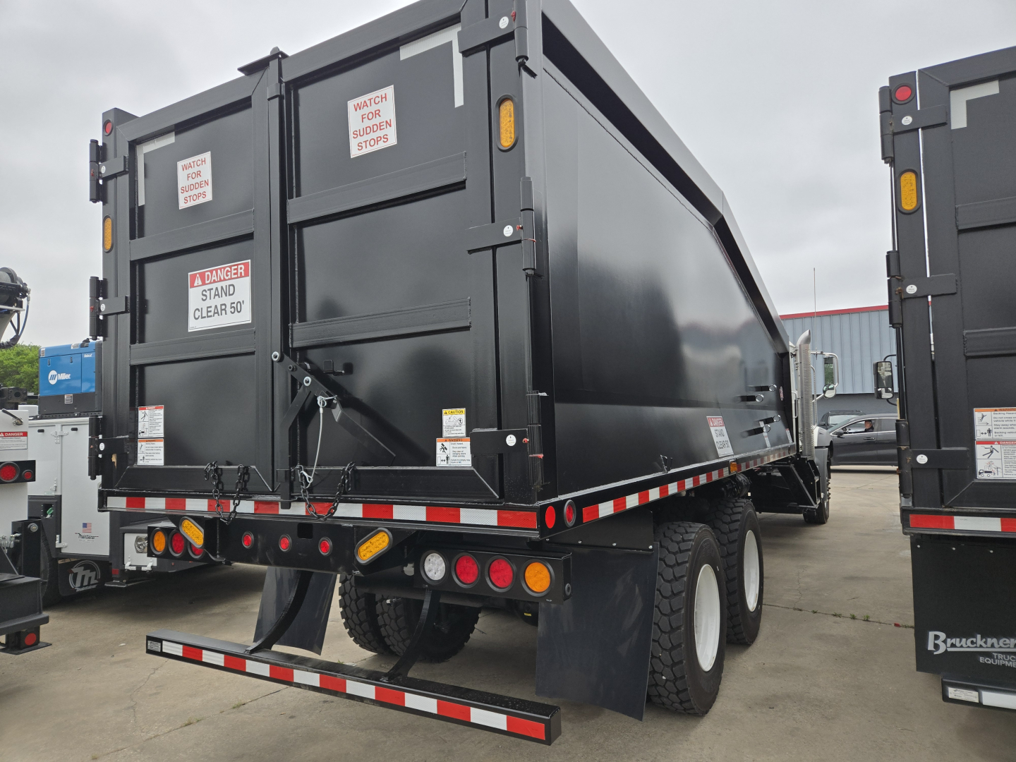 Rear view of a new Mack GR64B dump truck showing safety decals and rear underride guard.