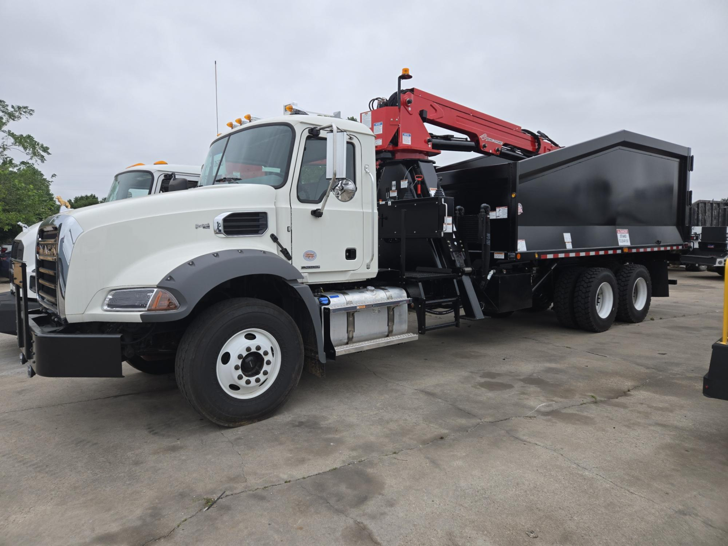 Mack GR64B truck with a red crane arm and a black dump bed, side view, white cab, gravel lot.