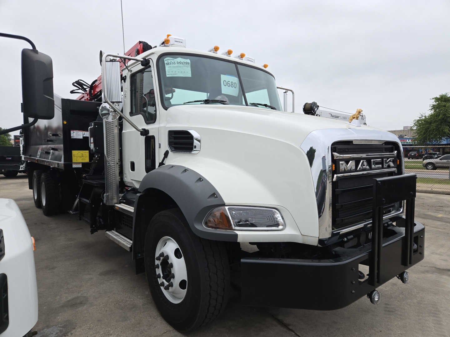 Mack GR64B heavy-duty grapple truck in white with front grille guard and amber beacon lights, side mirrors, and chunky tires; VIN sticker visible in windshield.