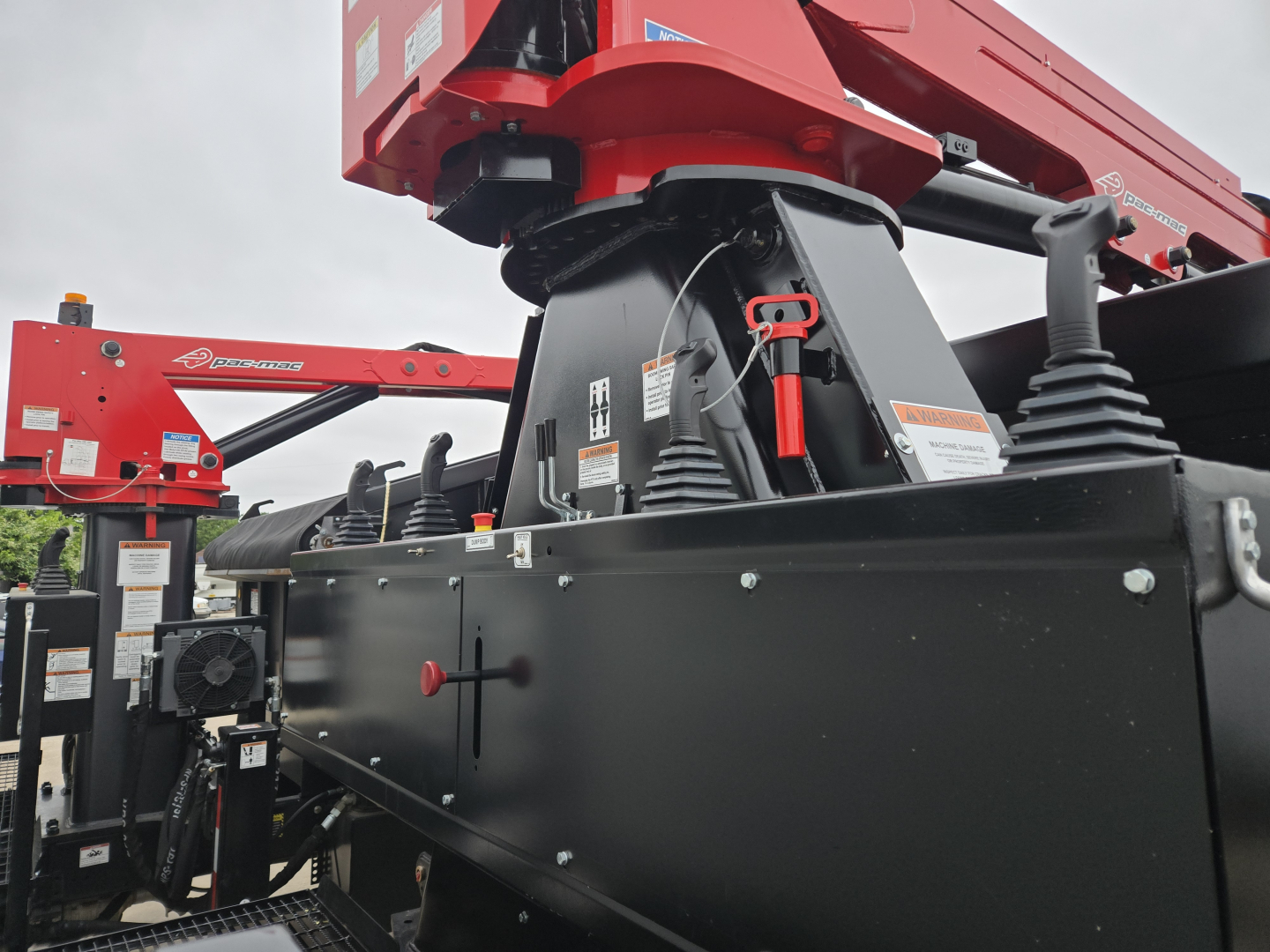Grapple truck chassis with red boom and black undercarriage; visible hydraulic components and safety labels on the side.