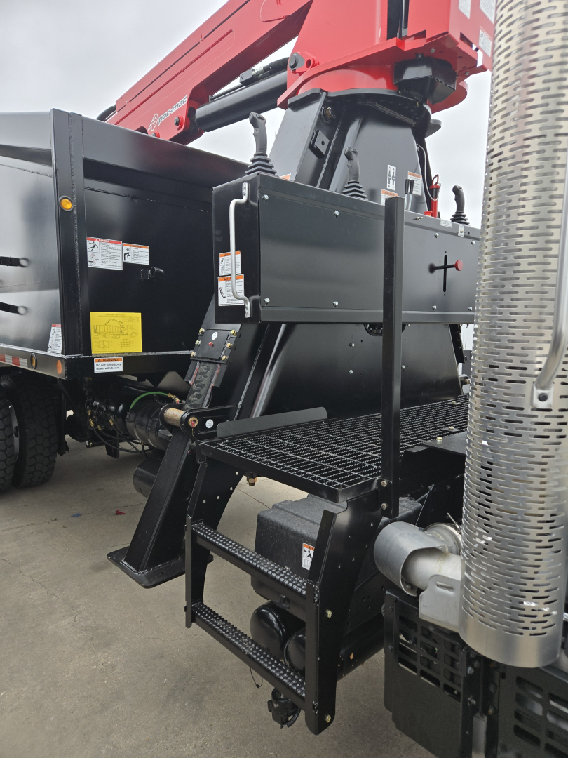 Mack GR64B truck chassis with a mounted hydraulic grapple arm and metal steps in foreground.
