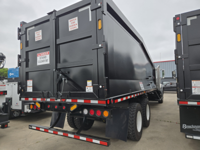 Rear view of a new Mack GR64B dump truck showing safety decals and rear underride guard.