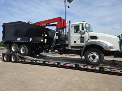 Mack GR64B truck with a red crane on a long lowboy trailer, white cab, grapple bed, side view showing loading equipment and dual rear axles.