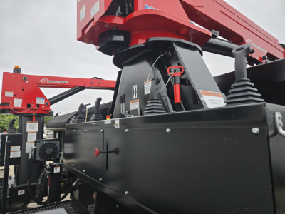 Grapple truck chassis with red boom and black undercarriage; visible hydraulic components and safety labels on the side.