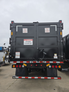 Rear view of a new Mack GR64B grapple truck showing warning decals and taillights.
