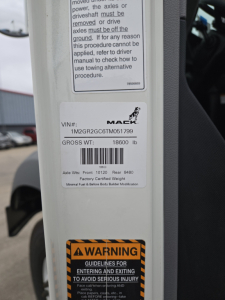 Mack GR64B VIN sticker label with VIN 1M2GR2GC6TM051799 and Gross Weight 18600 lb, safety warning label visible.