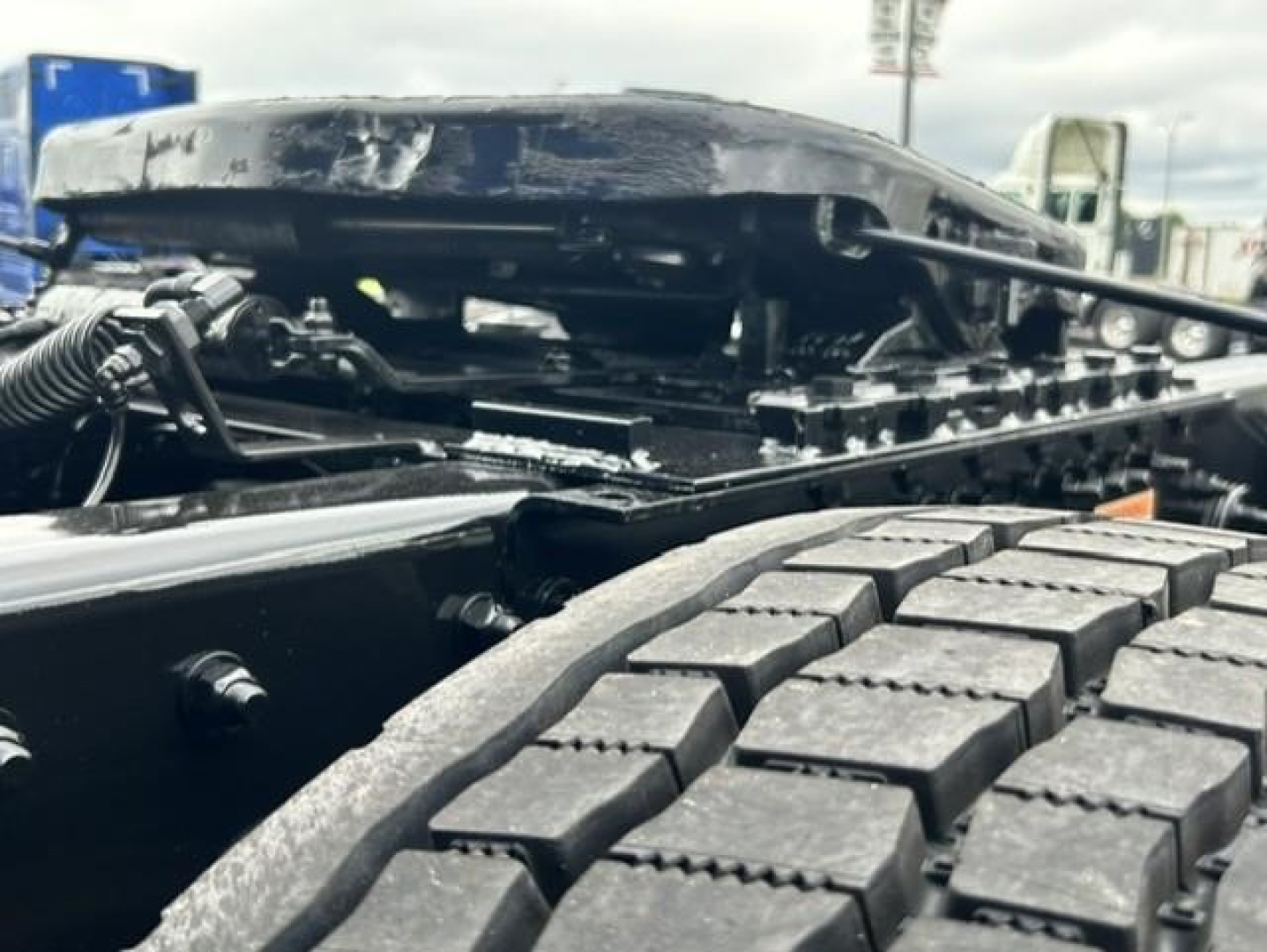 Truck engine bay view showing front wheel and engine components of a Freightliner Cascadia 126 tractor. Visible: air intake/hood area, tire tread, hoses, and metal framework.