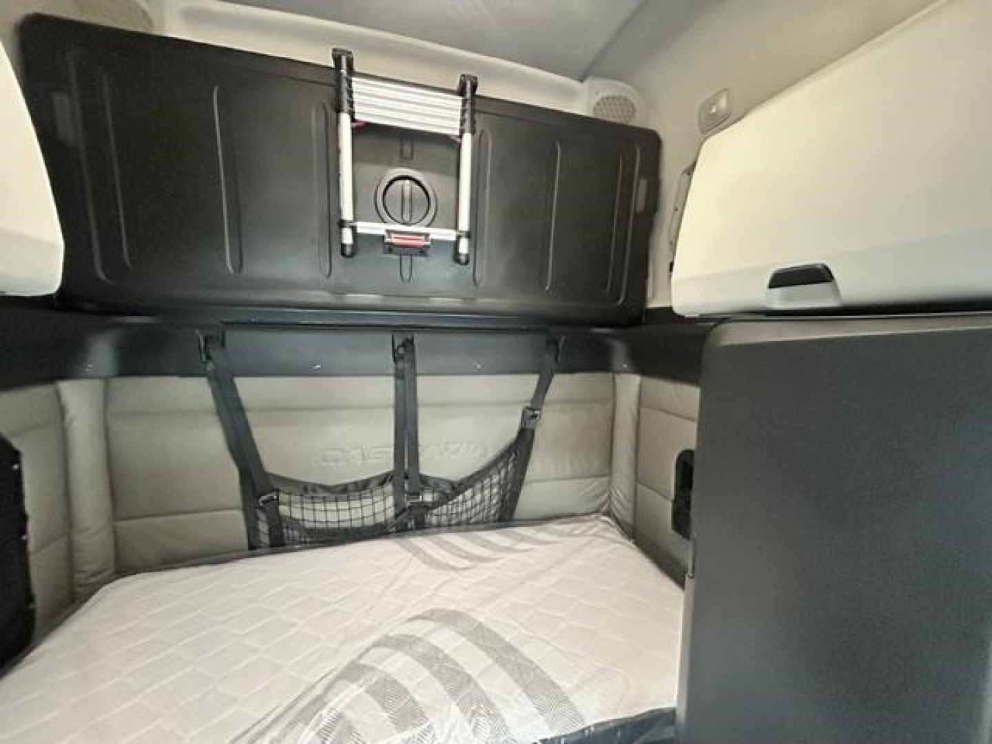 Freightliner Cascadia 126 sleeper cab interior showing bunk area with beige quilted mattress, straps, and storage nets.