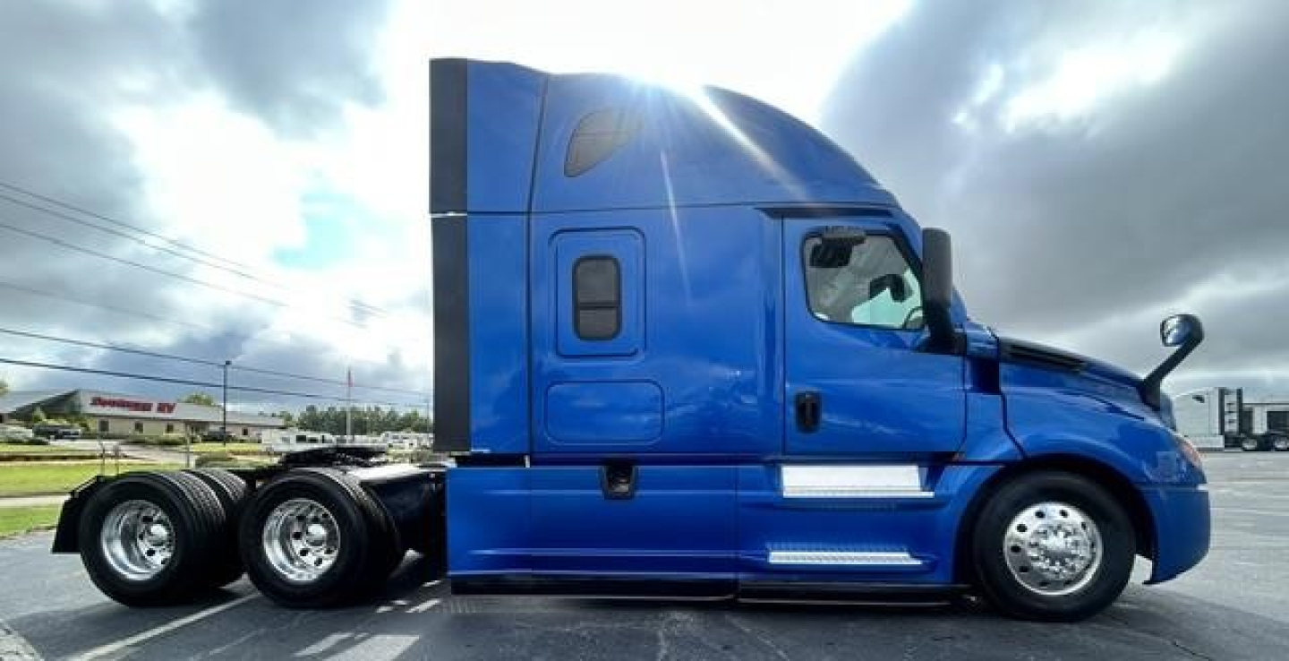 Truck side view showing a blue 2022 Freightliner Cascadia 126 sleeper tractor with dual rear axles and chrome wheels.