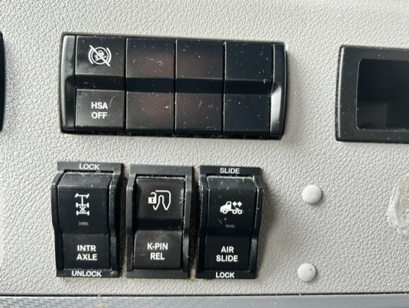 Controls panel in Freightliner truck showing HSA OFF switch block, lock/slide switches labeled INTR AXLE UNLOCK, K-PIN REL, AIR SLIDE LOCK, and vehicle icons.