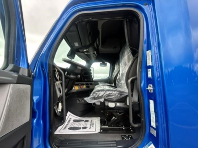 Truck cab interior of a blue 2022 Freightliner Cascadia 126, view of driver seat and dashboard with plastic covering on seat.