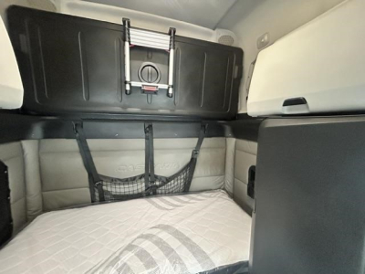Freightliner Cascadia 126 sleeper cab interior showing bunk area with beige quilted mattress, straps, and storage nets.