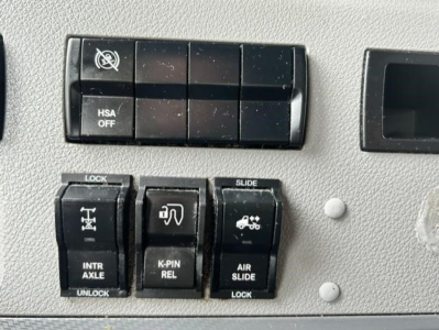Controls panel in Freightliner truck showing HSA OFF switch block, lock/slide switches labeled INTR AXLE UNLOCK, K-PIN REL, AIR SLIDE LOCK, and vehicle icons.