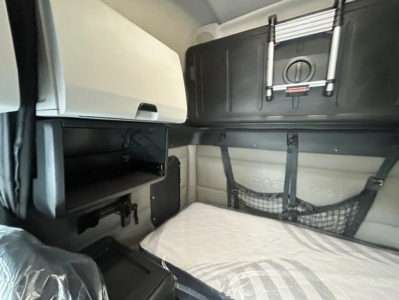 Interior sleeper cab of a Freightliner Cascadia showing bunk area with storage nets, side compartments, and a mounted panel.