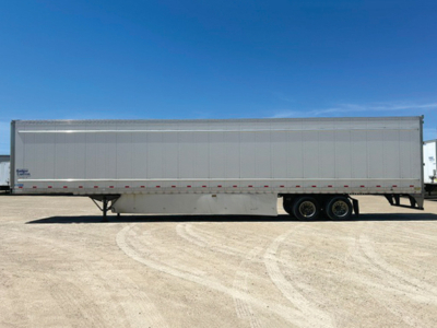 Trailer side view showing a white Stoughton dry van trailer with dual rear axles and landing gear, under clear blue sky.