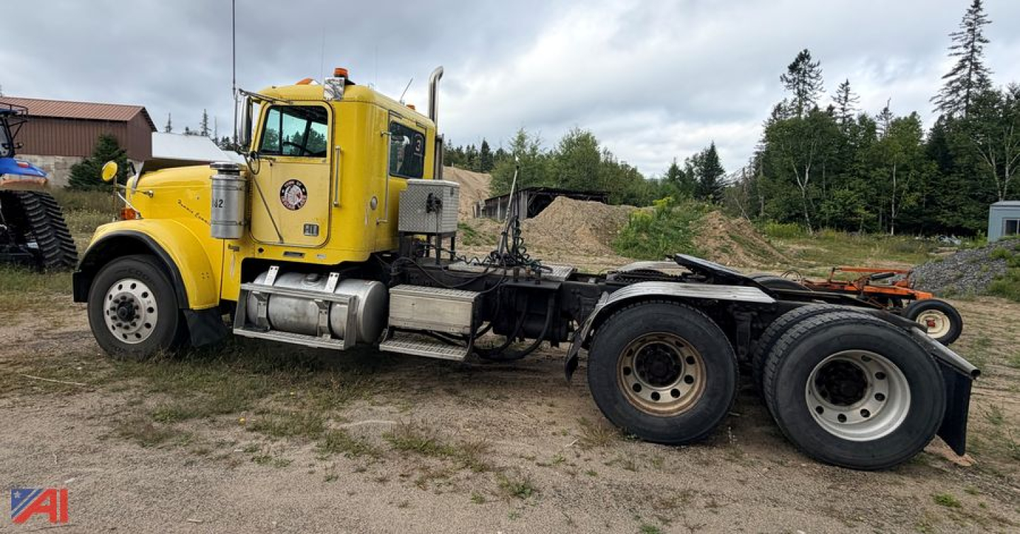 Tractor trailer chassis showing 3 axles and a yellow Freightliner cab with sleeper, visible fuel tanks, and exposed drivetrain.