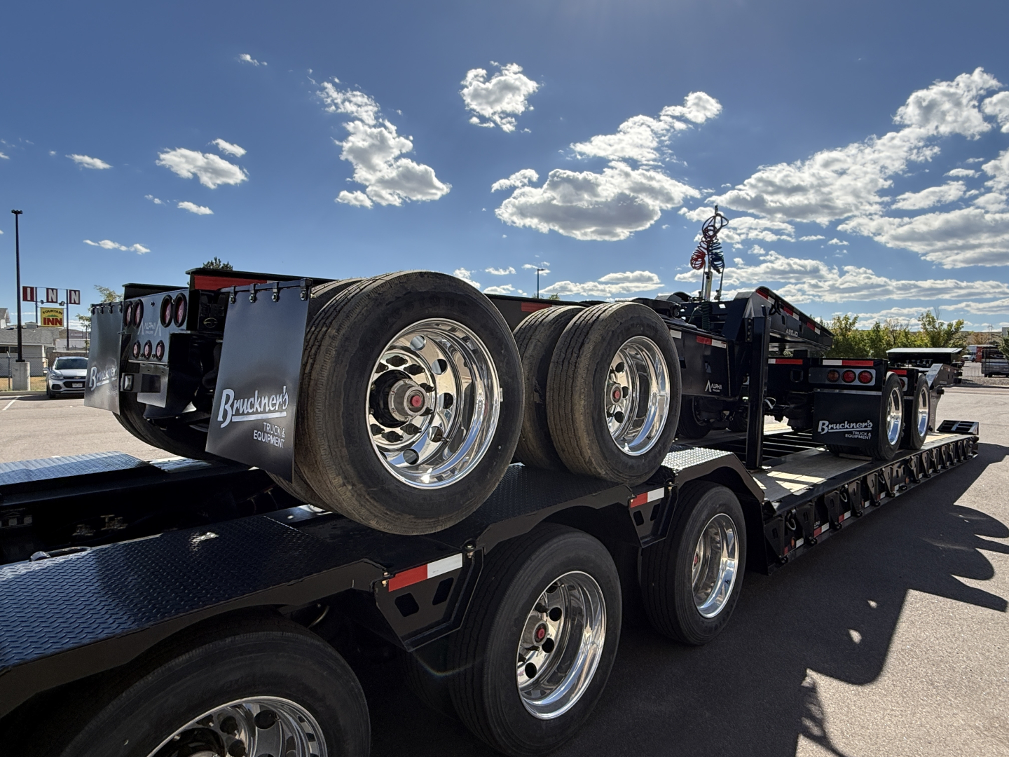 2027 Alpha A120HDG-SF2 lowboy trailer with dual rear axles and chrome wheels; on flatbed trailer with wheels and tires visible.