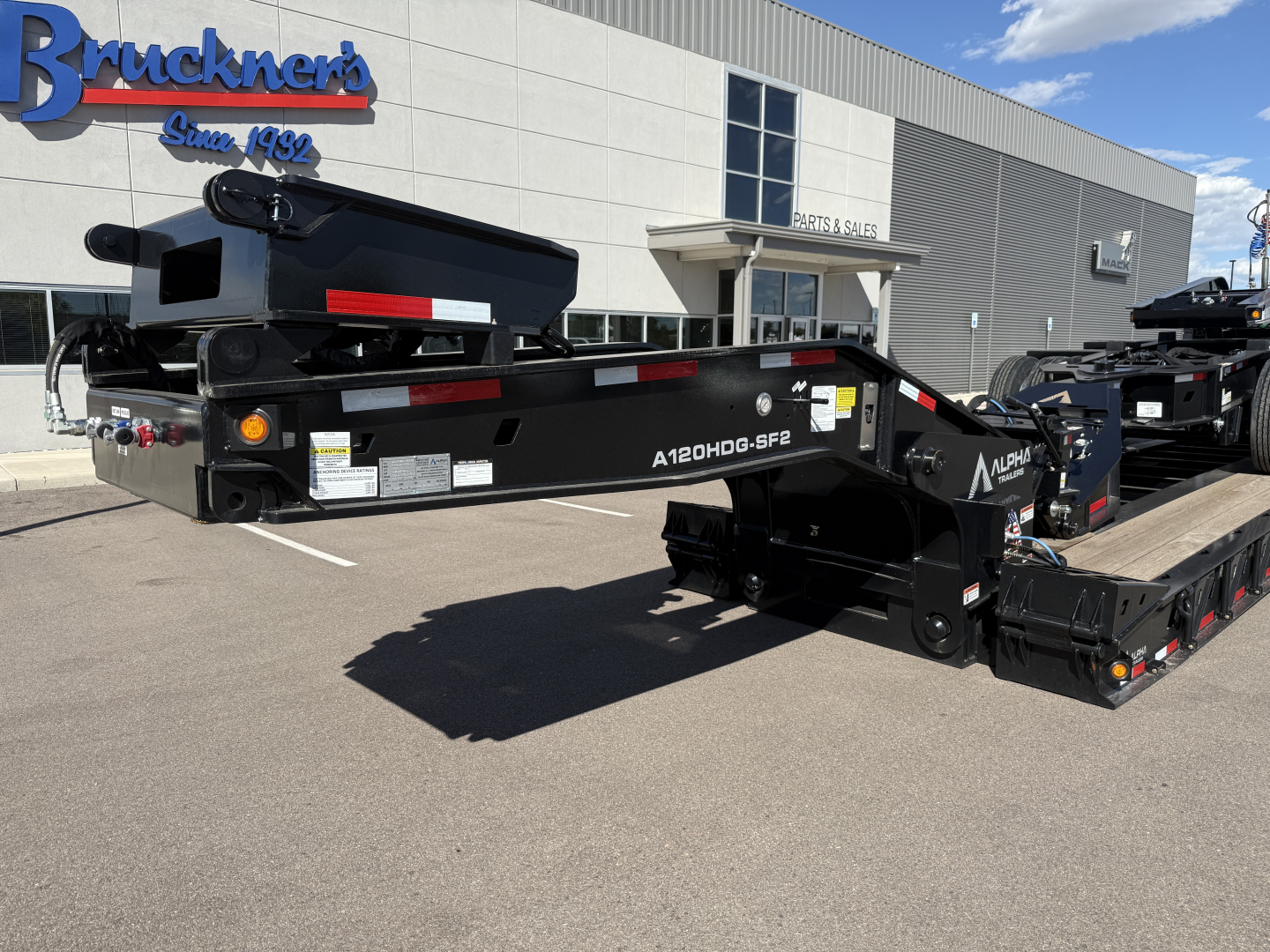 A black lowboy trailer with A120HDG-SF2 markings parked outside a dealership building.