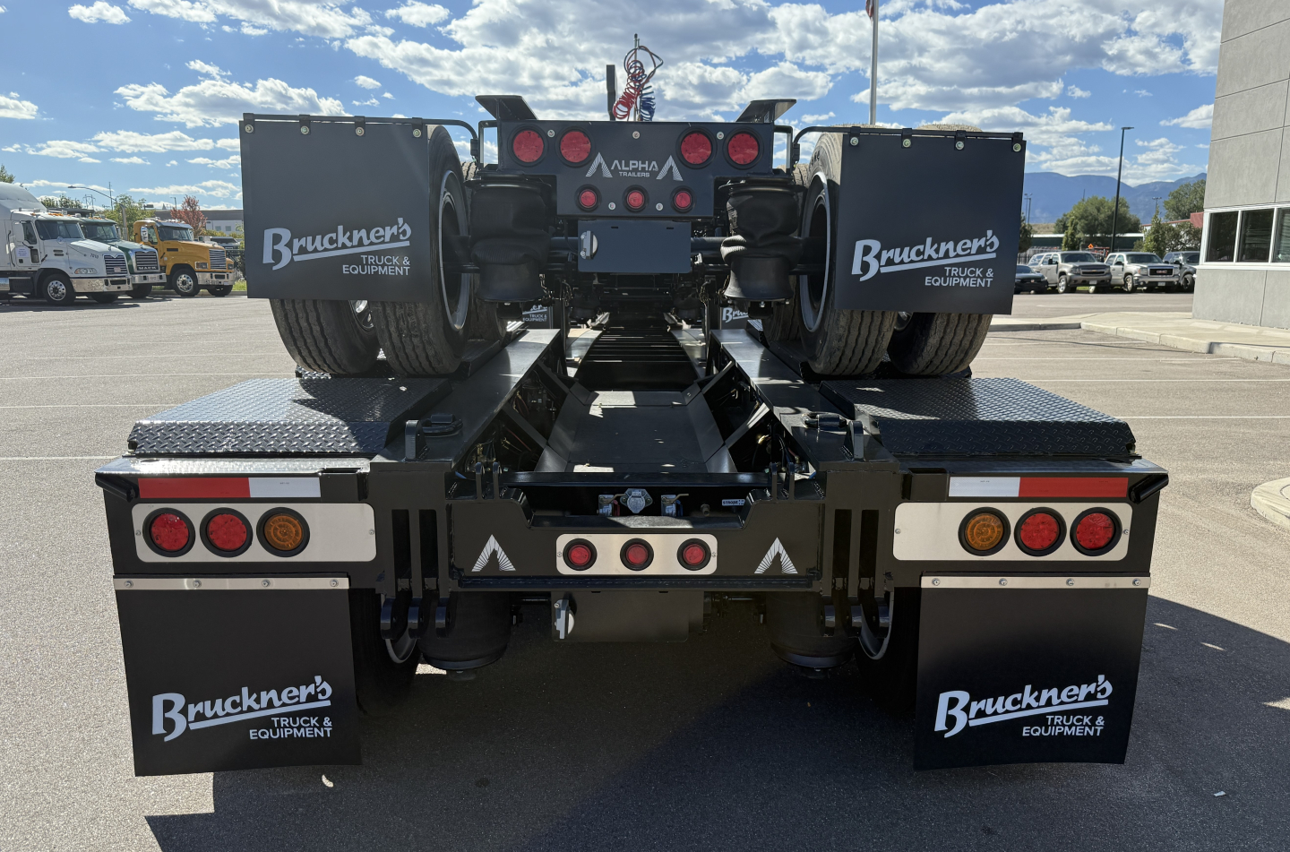 Rear view of a new 2027 Alpha A120HDG-SF2 lowboy trailer showing dual rear axles, black mud flaps with Bruckner’s logo, and reflective lights.