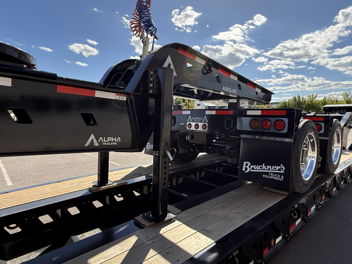 Trailer component showing Alpha A120HDG-SF2 lowboy trailer with black frame and rear axle assembly, branding including Alpha and Bruckner’s Equipment Truck logos.