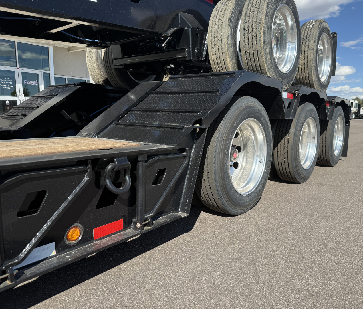 Trailer axle and dual tires of a lowboy trailer with multiple wheels and black painted frame.
