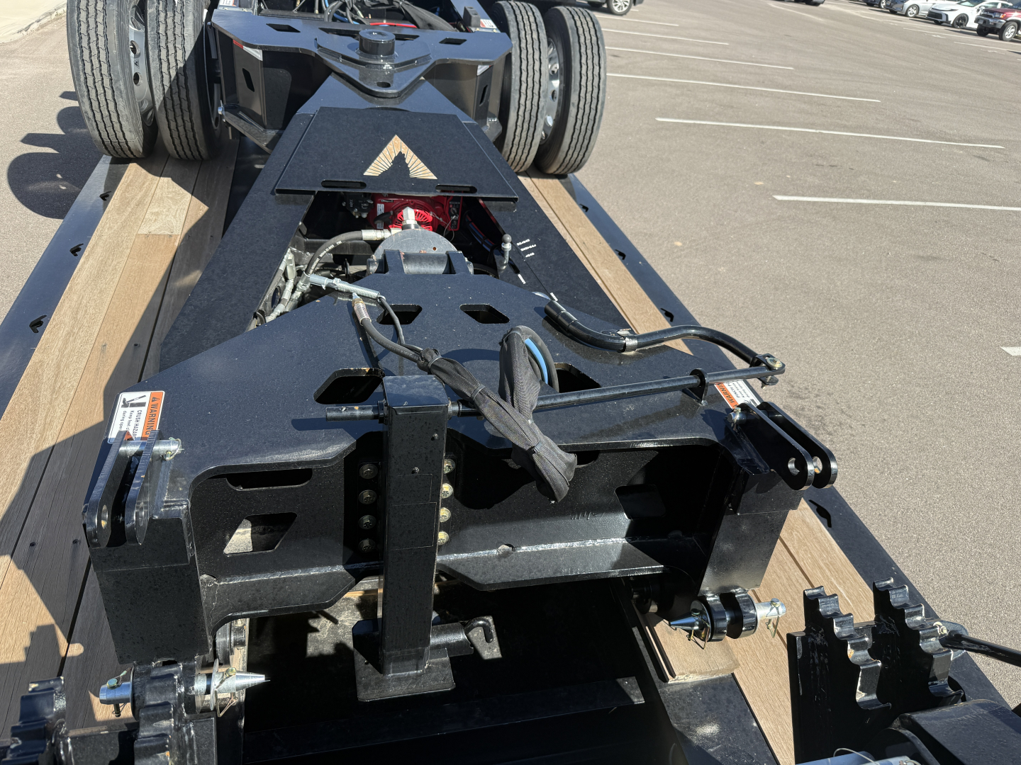 Trailer chassis and hitch area showing A-frame with wiring and connectors, dual rear tires, black metal frame, and wooden deck sections.