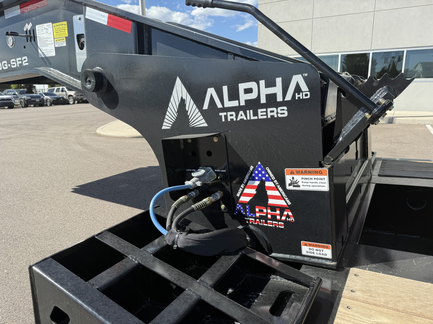 Alpha Trailers A-head deck showing Alpha HD logo and hydraulic hoses; side of lowboy trailer component with warning labels and text 'ALPHA HD TRAILERS' in white.