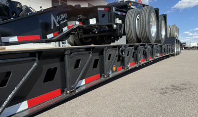 Lowboy trailer deck showing spare tires and structural side rails with reflective red/white stripes.