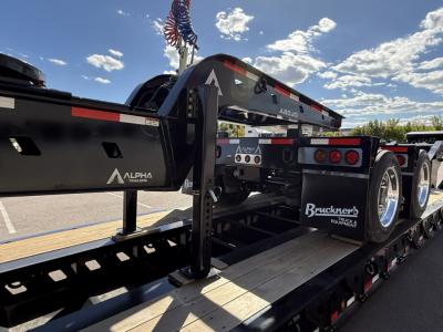 Trailer component showing Alpha A120HDG-SF2 lowboy trailer with black frame and rear axle assembly, branding including Alpha and Bruckner’s Equipment Truck logos.