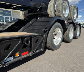 Trailer axle and dual tires of a lowboy trailer with multiple wheels and black painted frame.