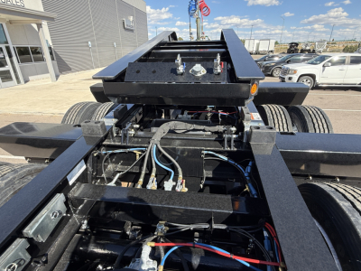 Trailer fifth wheel area showing hydraulic lines and electrical harnesses, black paint, chassis with two axles and suspension, mounting hardware, near front of a lowboy trailer.