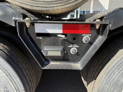 Trailer rear deck showing control panel with dash and gauges including 'RAISE' and 'LIFT AXLE' indicators, digital LCD display, and manual ride height knob on a lowboy trailer.