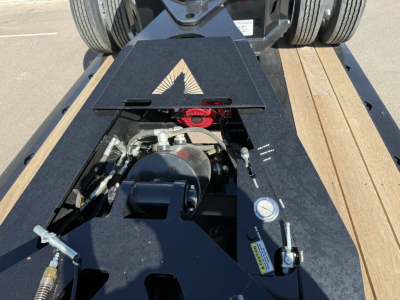 Trailer hitch area of lowboy trailer showing winch, hydraulic components, and deck with wooden planks; Alpha logo on black metal housing and various gauges and handles visible.