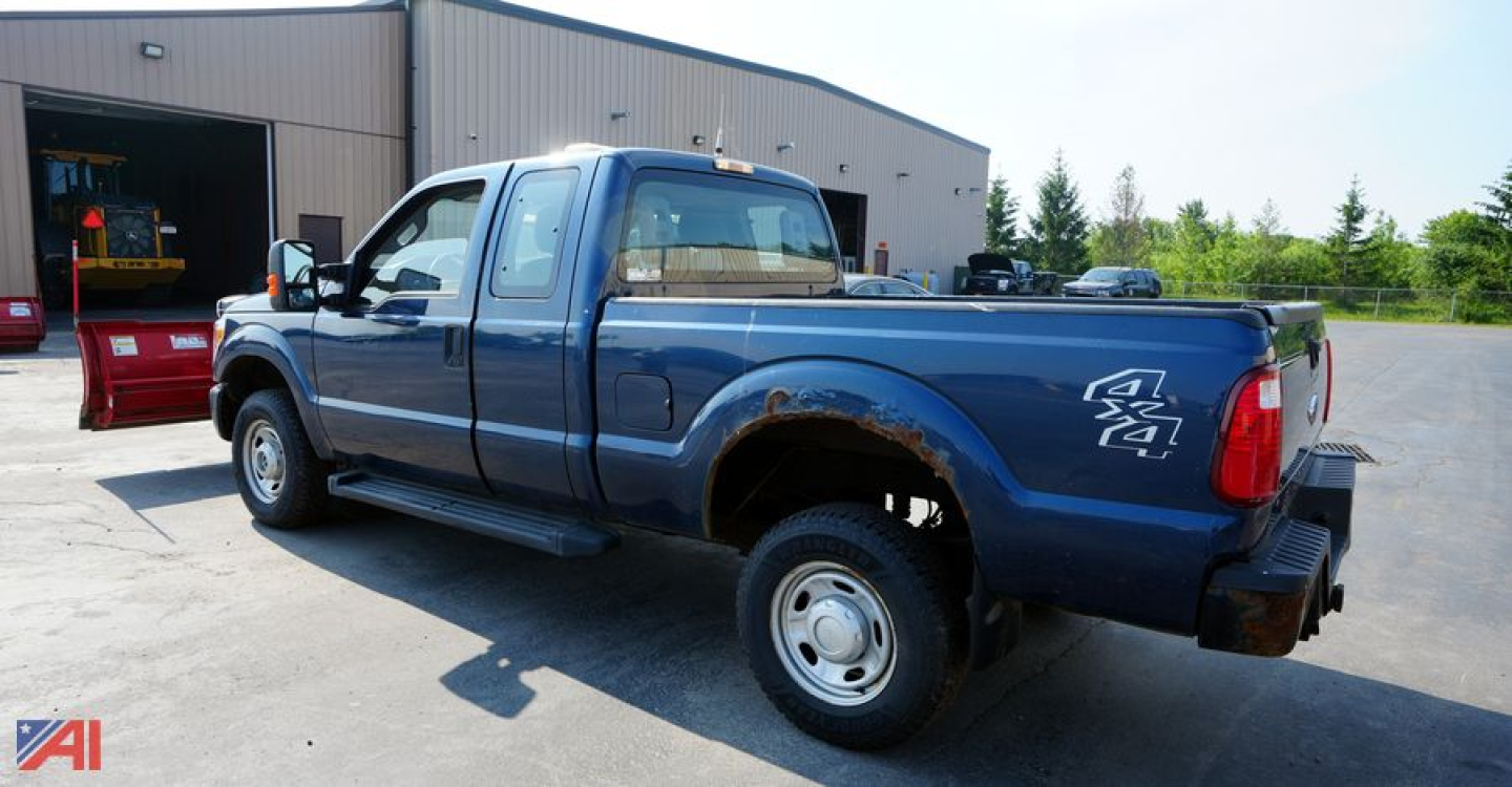 Ford F-250 extended cab pickup with plow attachment in blue, rear-side view showing 4x4 badge, long bed, and side steps.