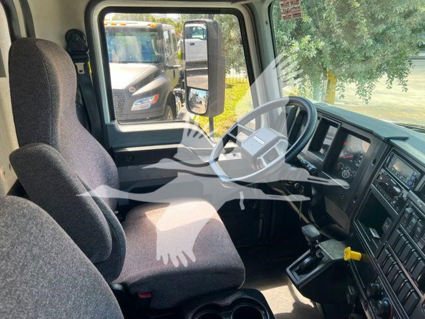 Truck cab interior showing driver seat, steering wheel, gear shifter, and dashboard in a Mack MD6. Visible window reflection of another truck.