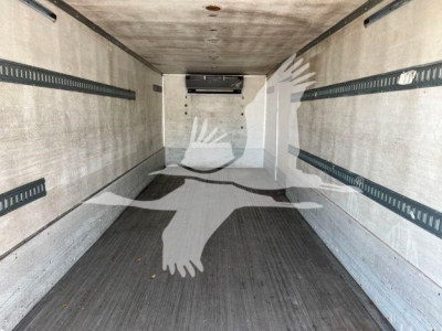 Truck interior showing empty refrigerated cargo area with white walls and black rubber floor, side rails and rear doors visible.