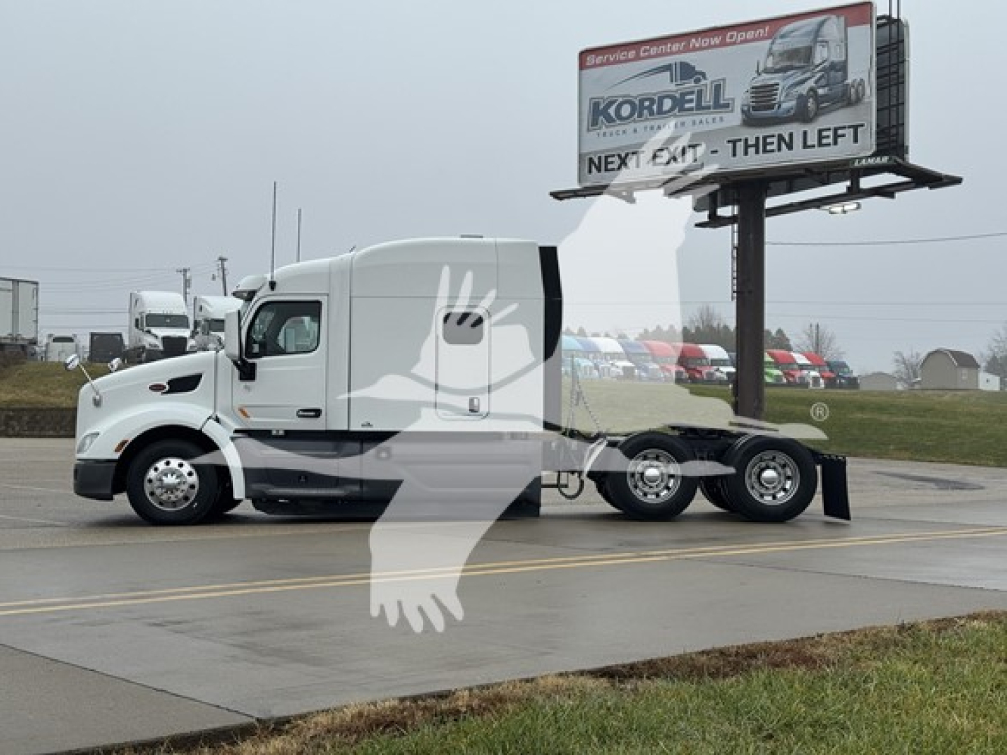 Peterbilt 579 conventional sleeper truck with a white cab and black accents, parked on road with billboard in background.