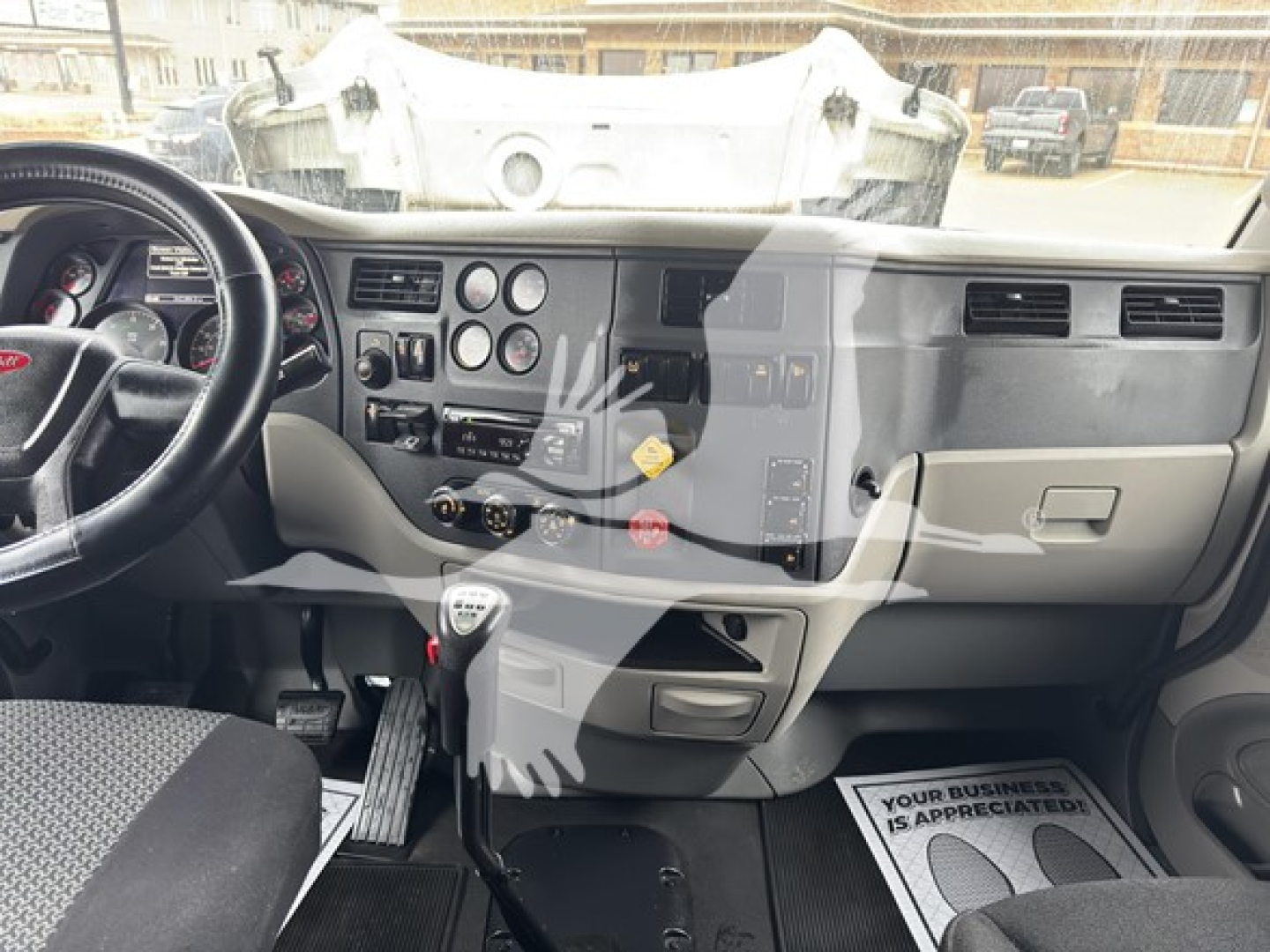 Peterbilt 579 cabin interior with steering wheel, dashboard gauges, gear selector, and driver-side floor mat in view.