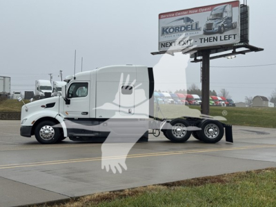 Peterbilt 579 conventional sleeper truck with a white cab and black accents, parked on road with billboard in background.