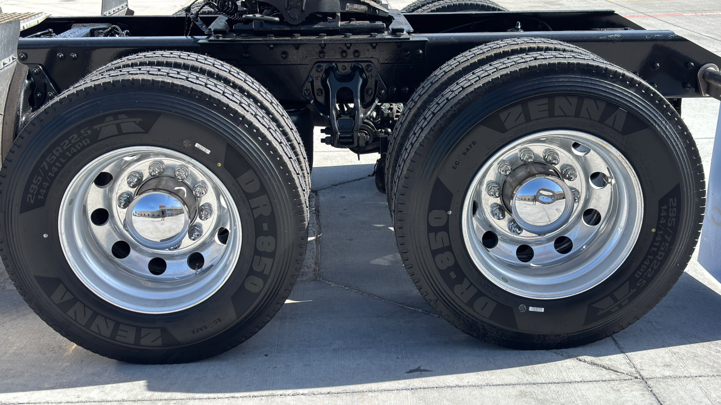 Kenworth T680 rear dual-axle wheel area showing dual tires with Bridgestone or similar brand, chrome hub covers, and suspension components.