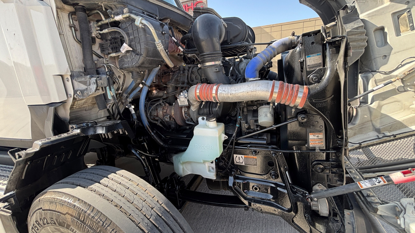 Kenworth T680 engine bay showing coolant reservoir and various hoses and components.
