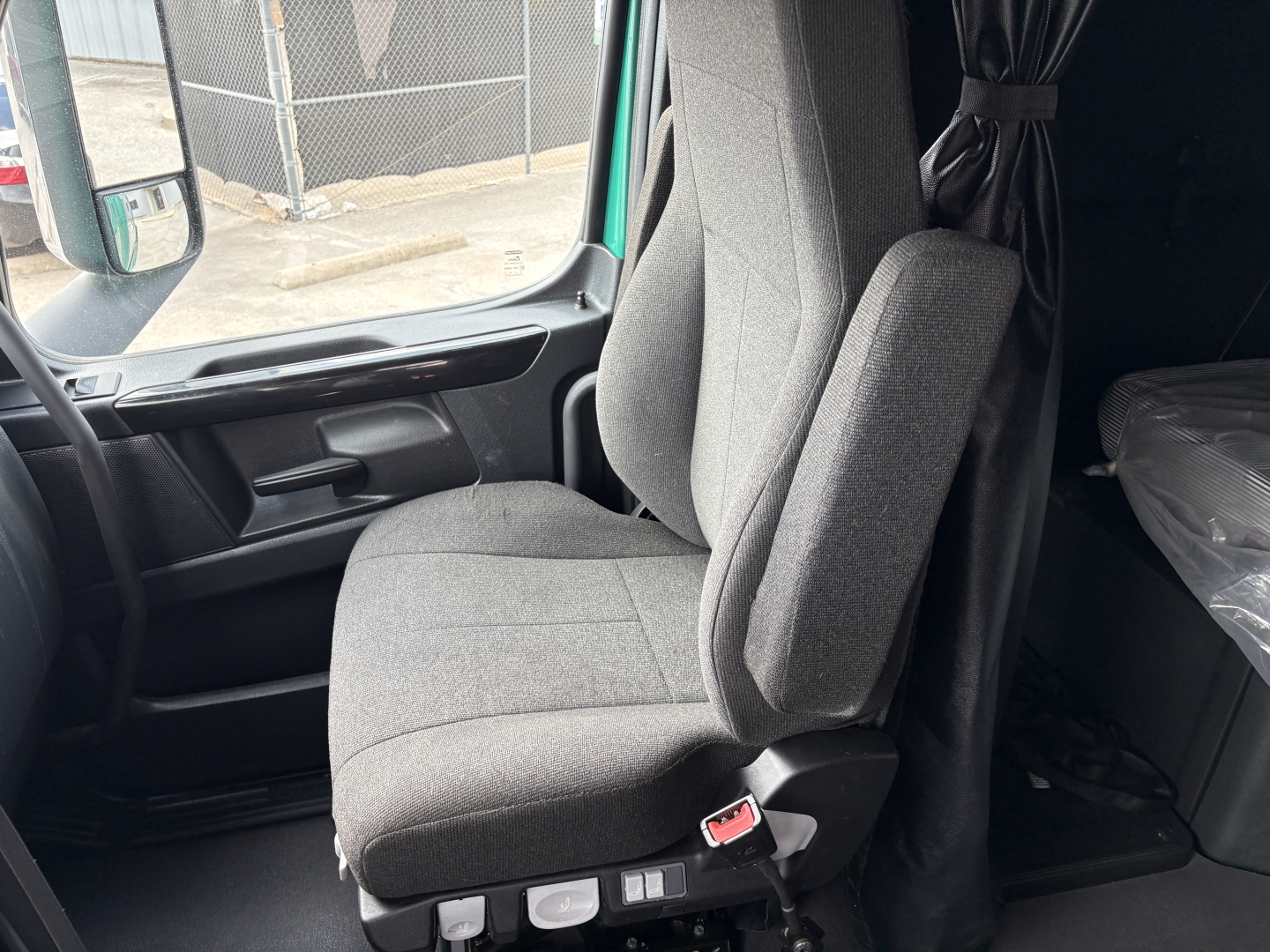 Truck cab interior showing the driver seat and passenger seat with grey fabric and armrests; window and door panel visible.